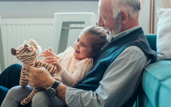 A grandfather with his granddaughter on his lap. The granddaughter is holding a stuffed tiger.