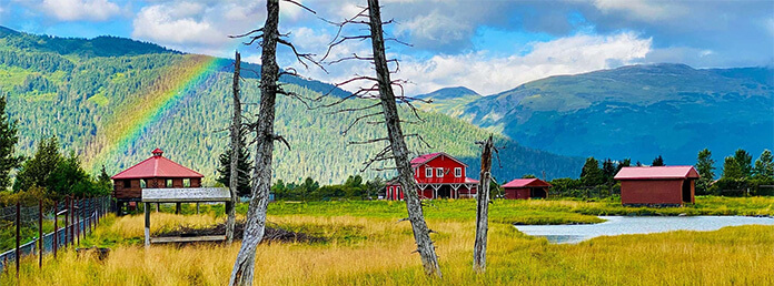 A scenic Alaskan countryside view featuring a red barn and mountain backdrop