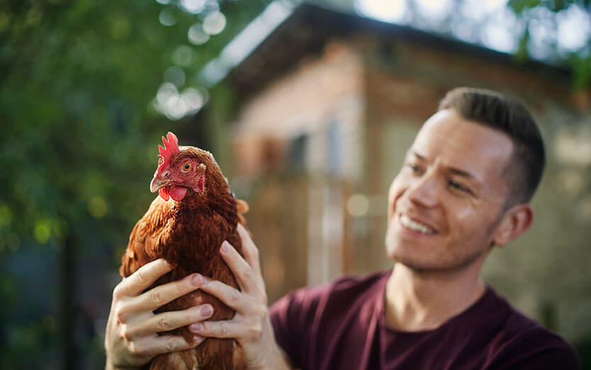 A smiling farmer holding a hen outside.
