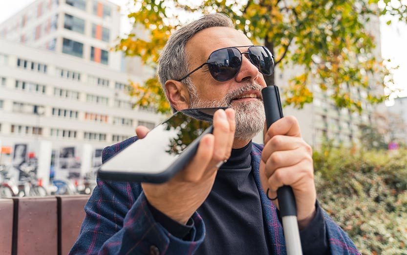 Man sitting on a bench holding a cane and talking on his cell phone