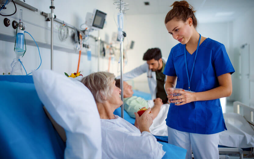 a nurse talking with a senior woman in a hospital bed post-operation