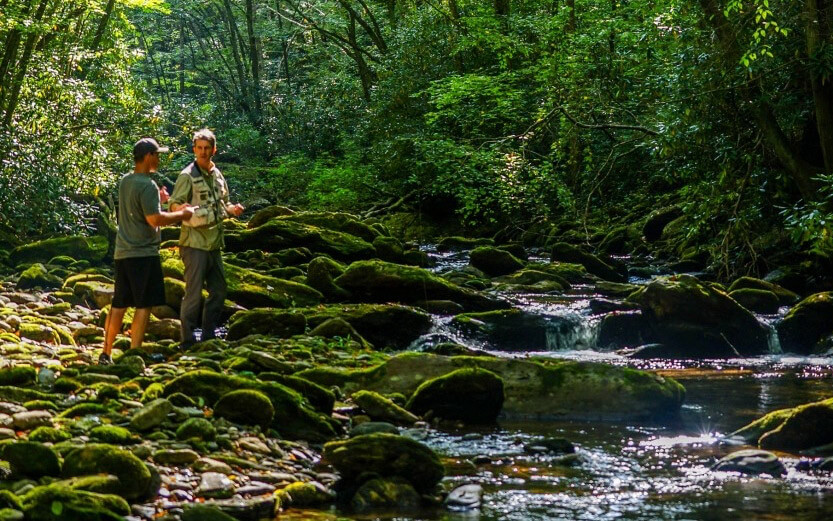 two men talking to each other next to a beautiful river
