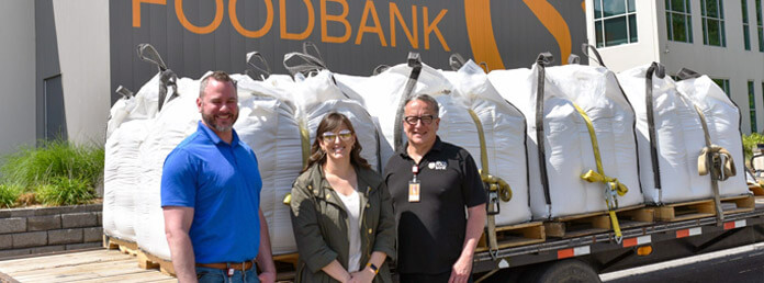 three people outside with food supplies on a truck bed