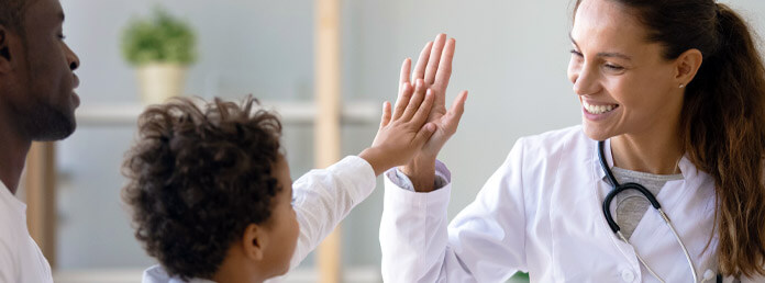 a doctor smiling and high-fiving a young patient who is sitting his father's lap