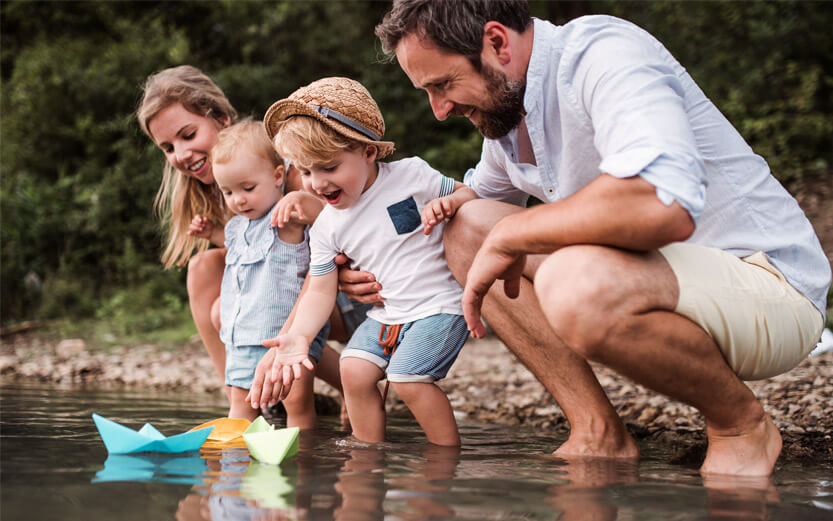 a family of four floating paper boats in a stream