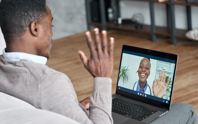 a man sitting on his couch waving and talking to his doctor via telehealth