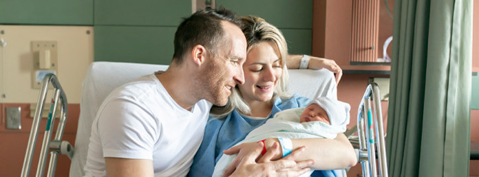 new parents sitting on a hospital bed smiling and admiring their newborn