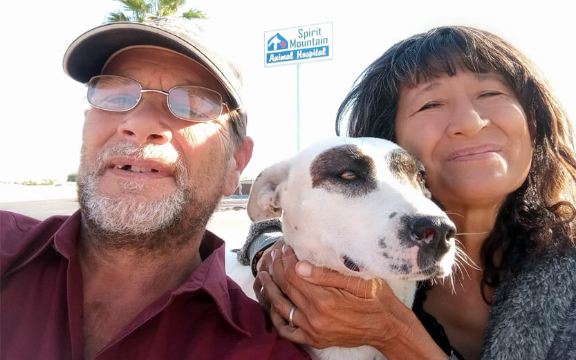 a couple smiling with their white and black dog outside an animal hospital