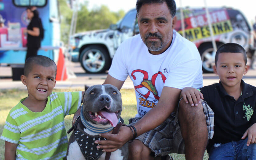 a father with his two sons kneeling down with their cute pit bull dog