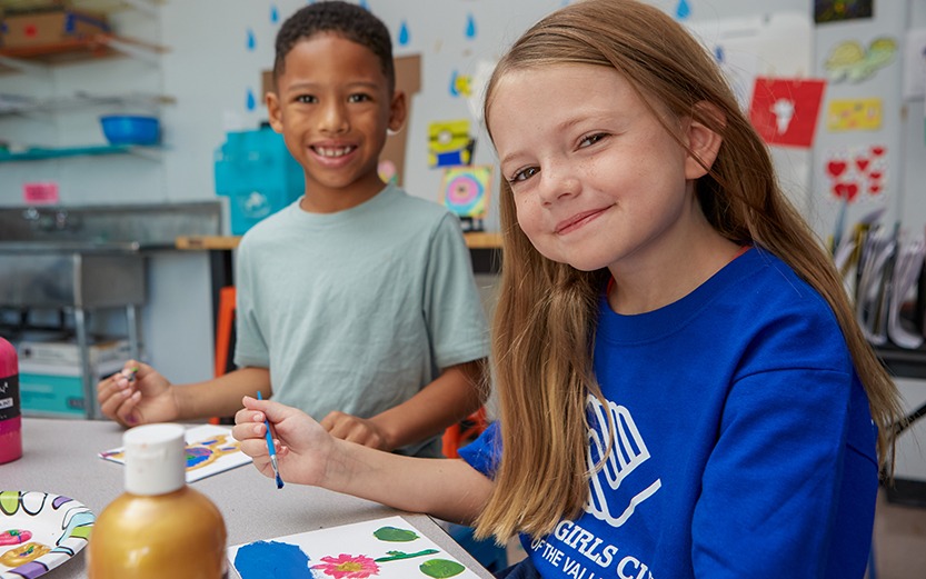 A boy and girl at a table, painting pictures and smiling