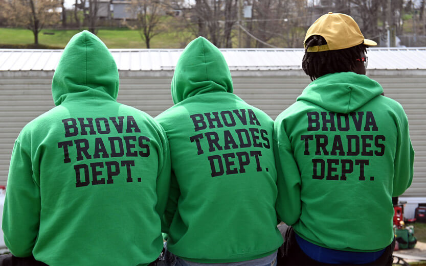 view from behind of three teen boys wearing green hoodies that read BHOVA Trades Dept.