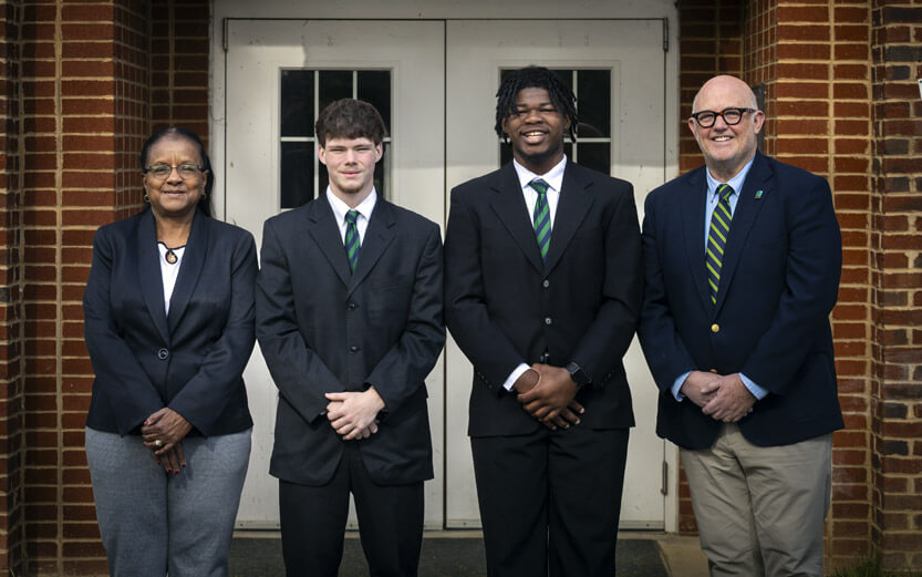 two adults and two teen boys wearing suits pose for a portrait