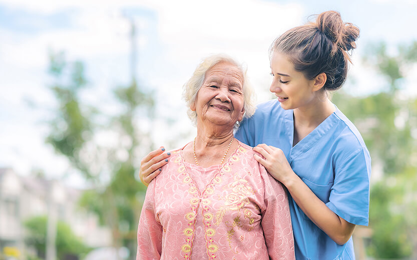 Smiling nurse caregiver take care of Asian elderly woman outdoor in the park