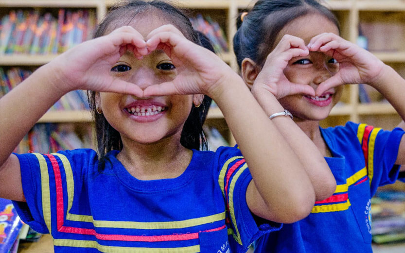 two school girls making hearts with their hands