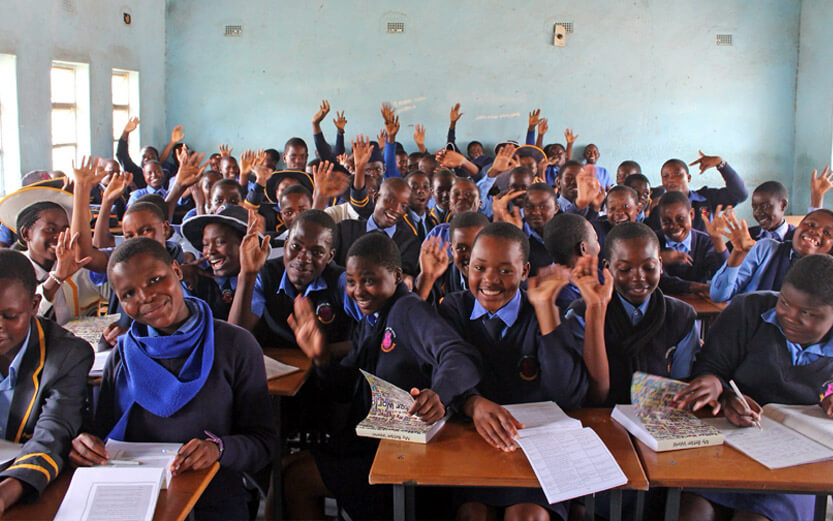 a classroom full of students smiling and raising their hands