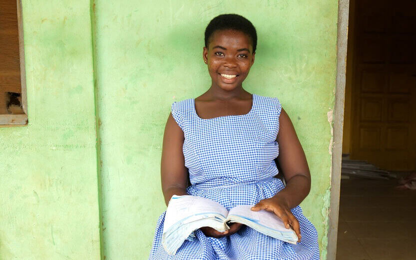 a student in a blue gingham dress reading a book while seated in front of a green wall