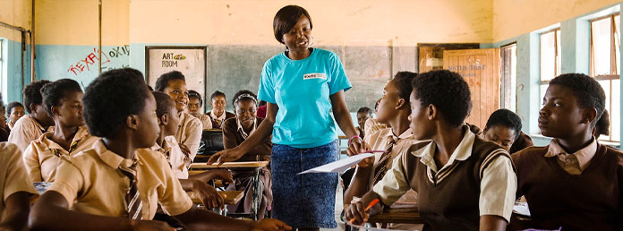 a teacher in a blue tshirt talking to students in the classroom
