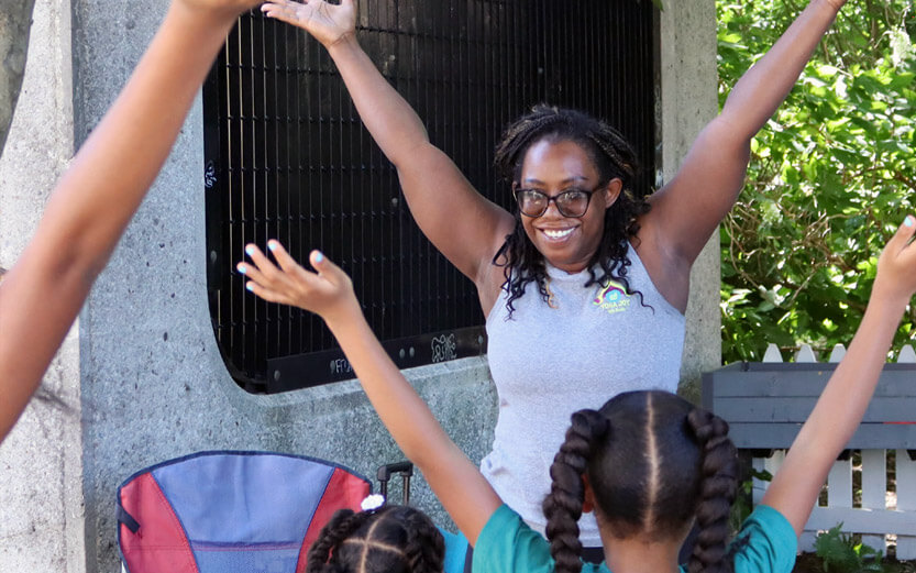 a woman standing in front of a group of children smiling and holding her arms up