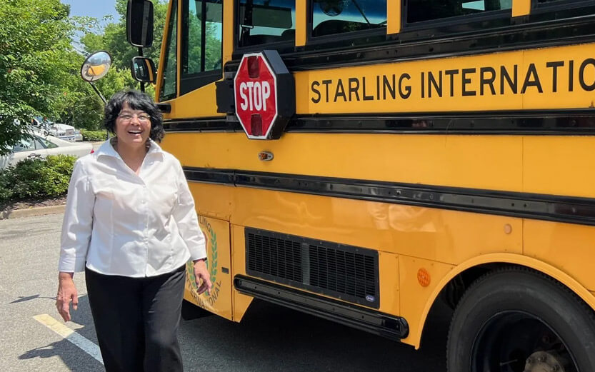 a woman smiling next to a yellow school bus