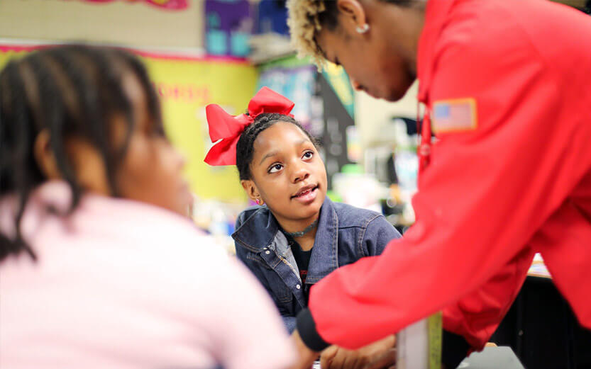 student looking up at a City Year volunteer helping them with schoolwork