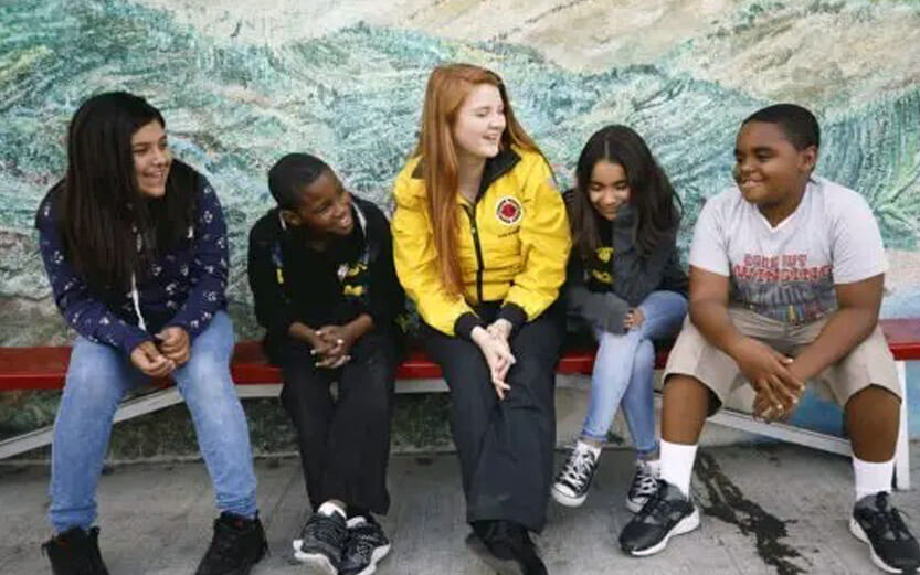 City Year volunteer in a yellow jacket sitting on a bench talking with students