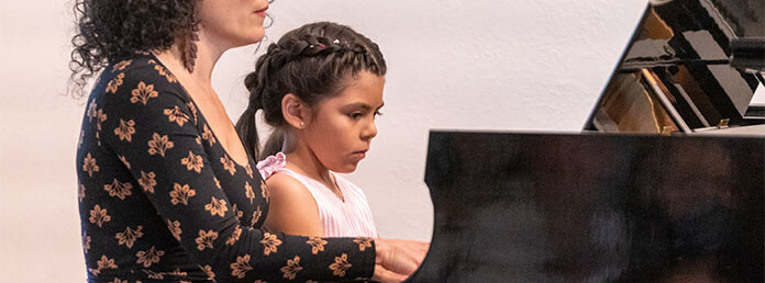 a woman sitting next to a little girl playing a piano
