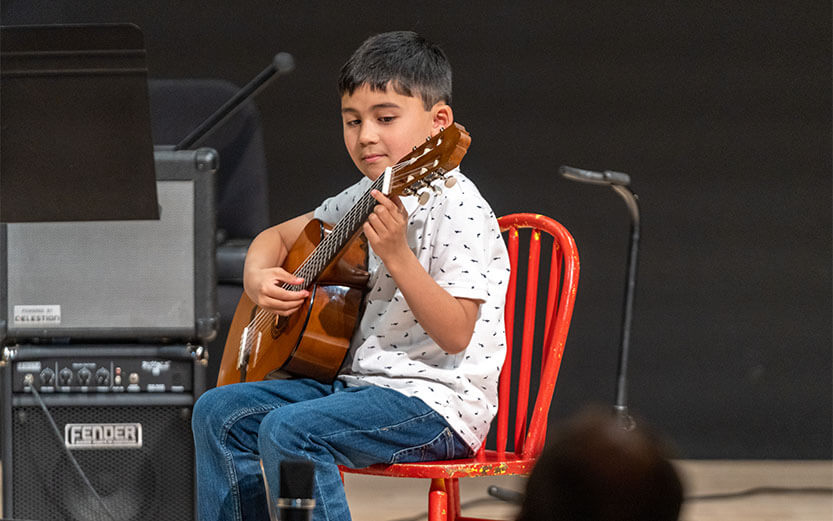 a boy sitting on a red chair playing a guitar