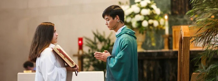 altar server holding a book open for a young minister to read from