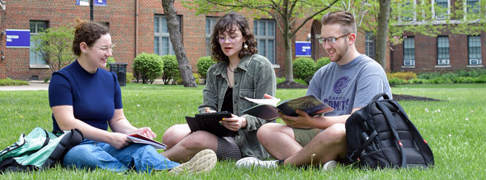 three students studying on the campus lawn