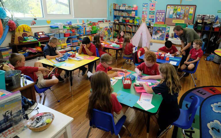 classroom filled with young children and their teachers, actively engaged in various learning activities at different tables