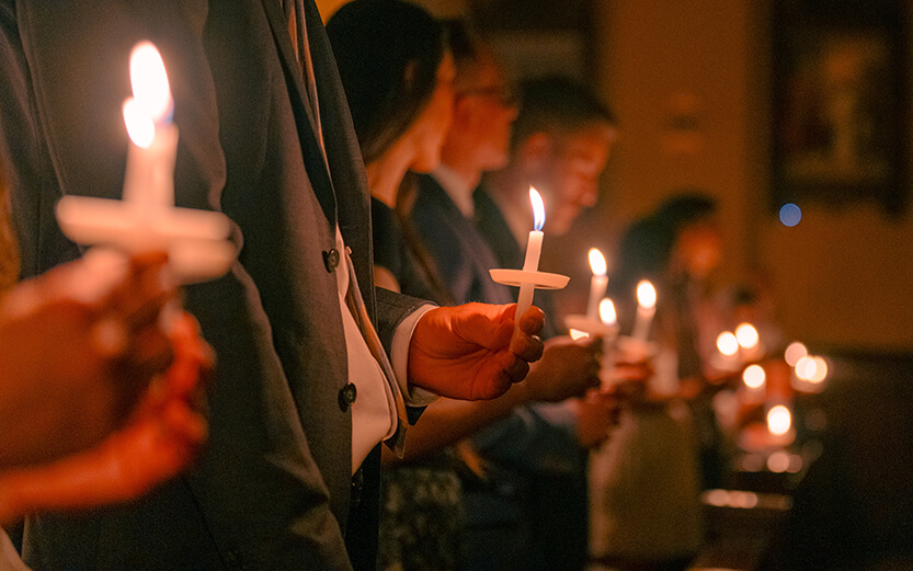 a congregation of people holding lit candles with paper drip protectors during a church service
