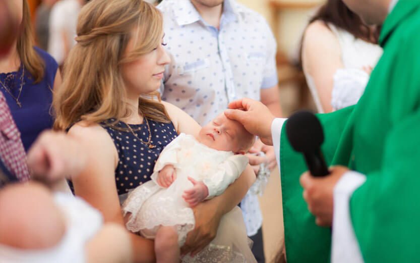 a woman holds her baby as a priest touches its head