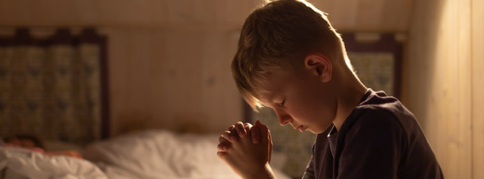 a young boy praying at his bedside