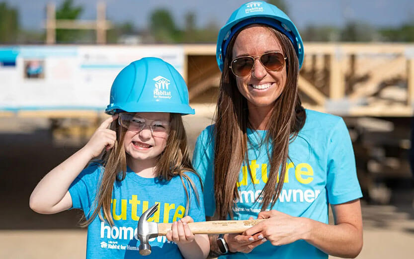 A young family holding a hammer in front of a new home construction site.