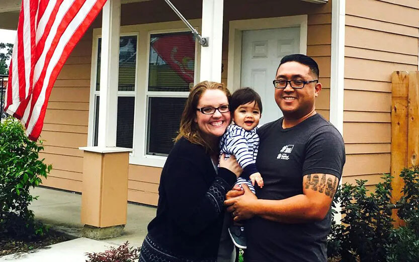 A young family smiling in front of a new home.
