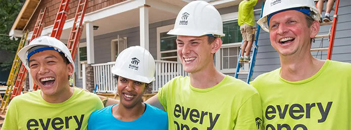 A group of adults hugging and smiling in front of a new home build.