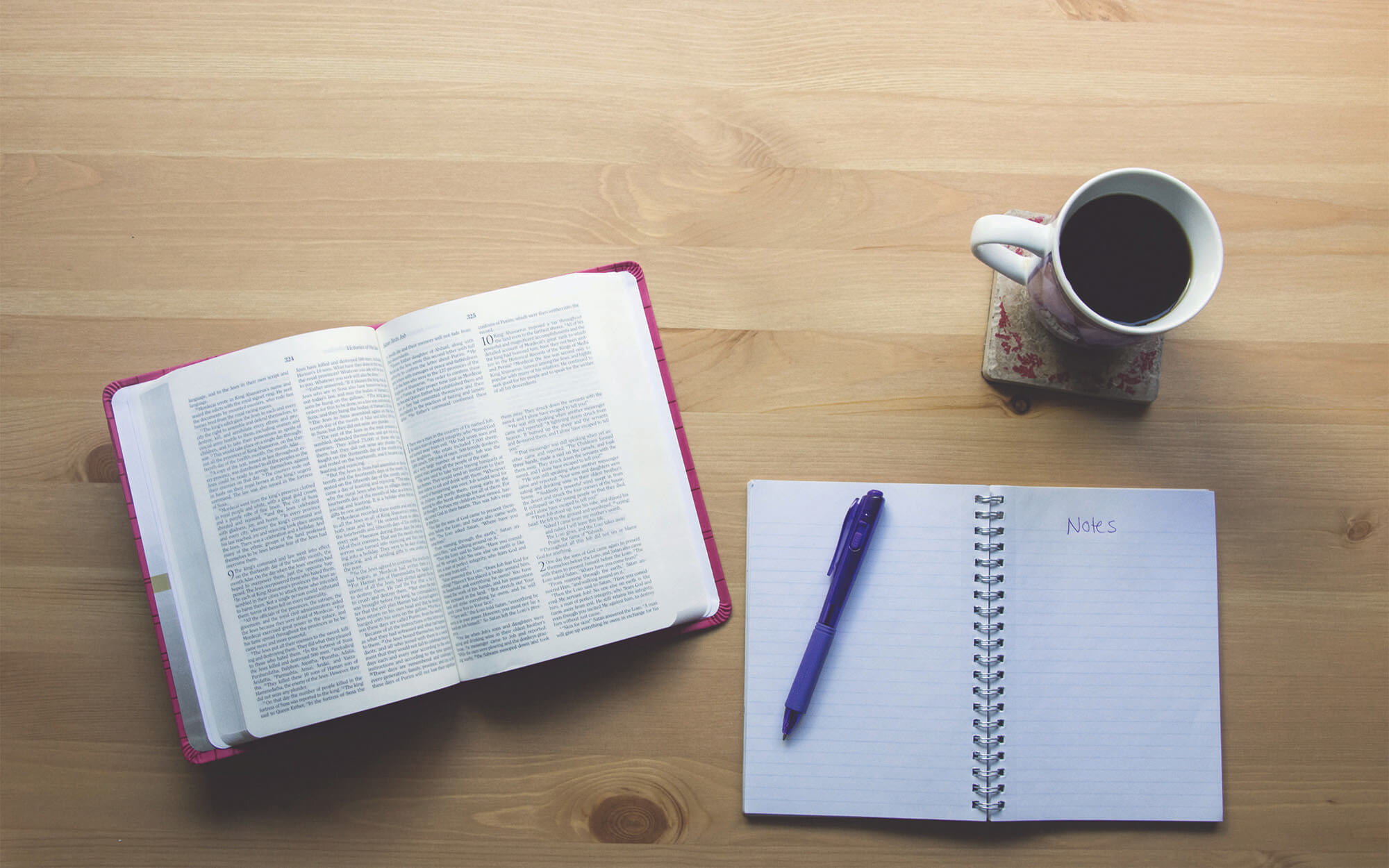 An open Bible next to a cup of coffee and a notebook