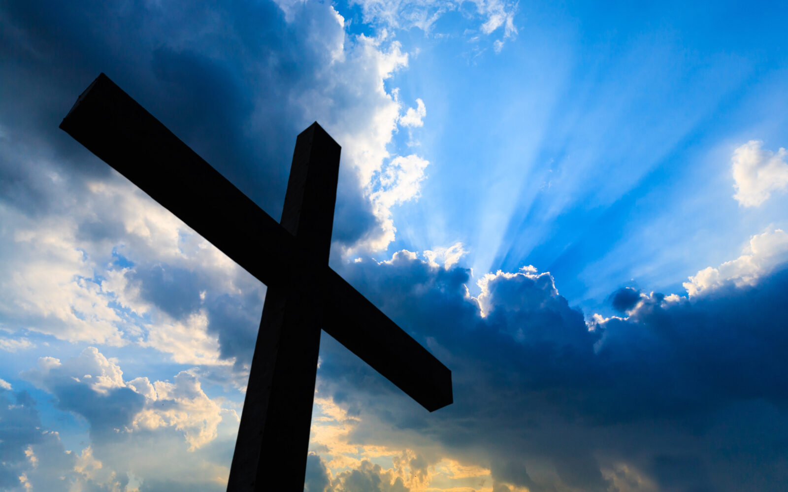 Silhouette of a cross against a blue sky with clouds