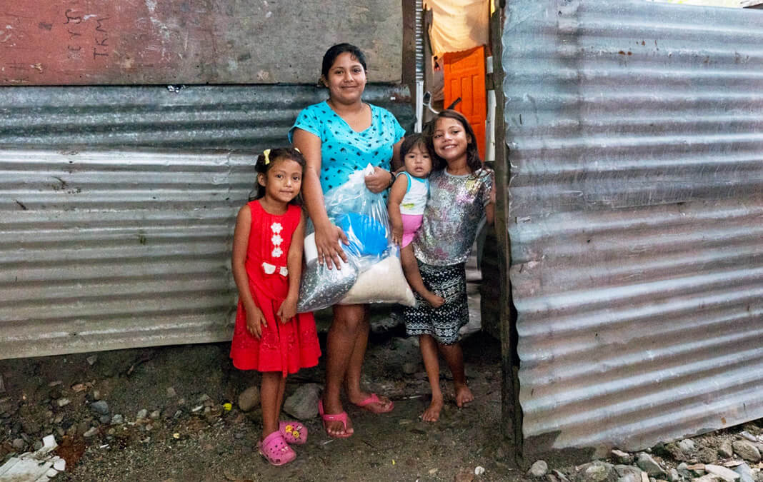 mother and children outside their aluminum home holding food supplies