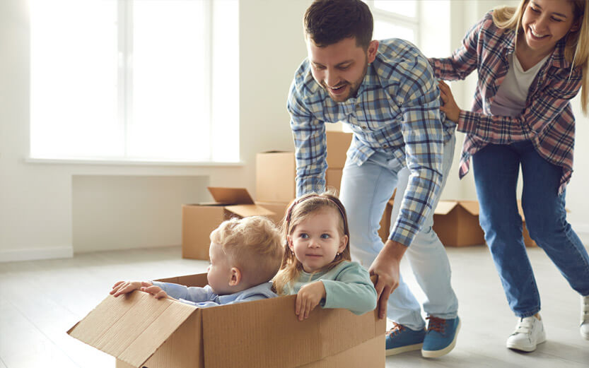 mom and dad pushing their toddlers around the living room in a cardboard box