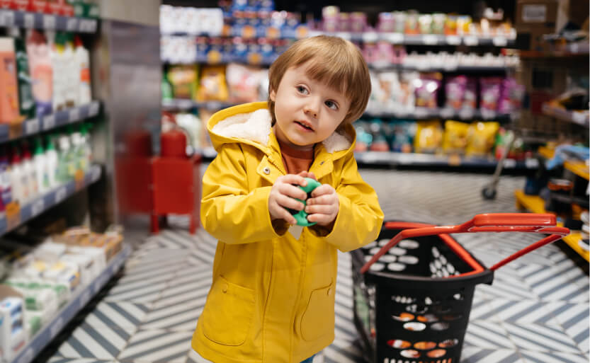a little boy in a yellow jacket standing in a grocery store aisle