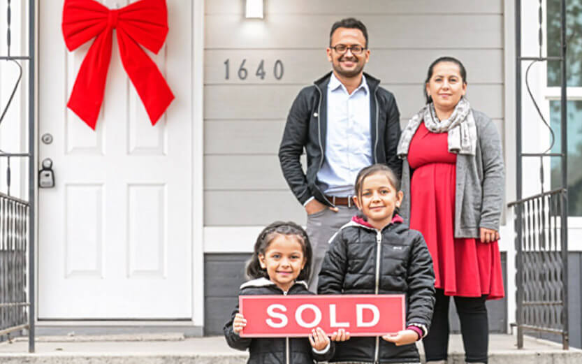 a family of four standing in front of their new home smiling
