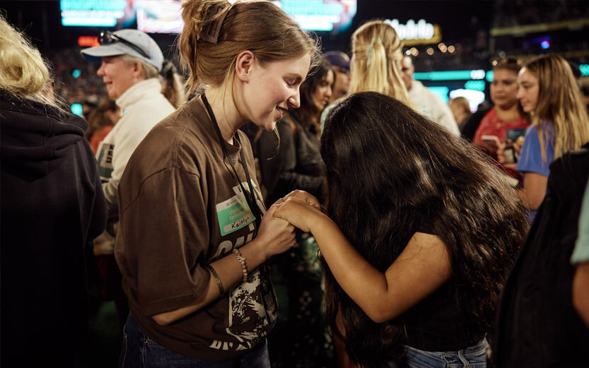 two young women holding hands and praying together