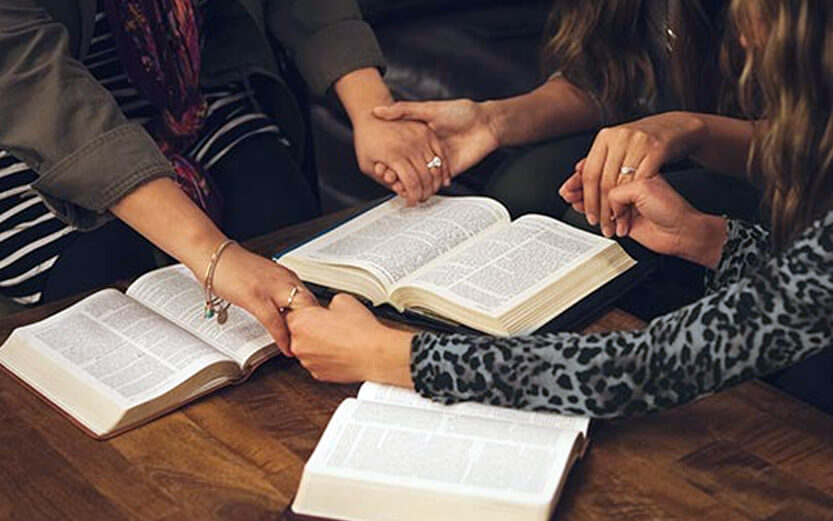 three women holding hands at a bible study