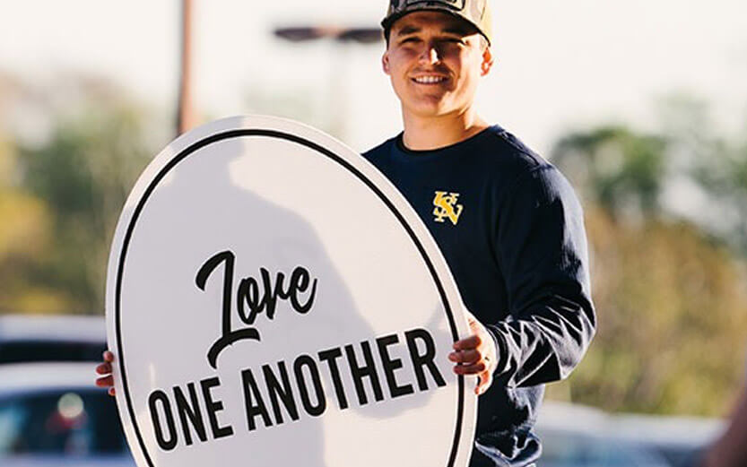 man holding a sign that reads Love One Another