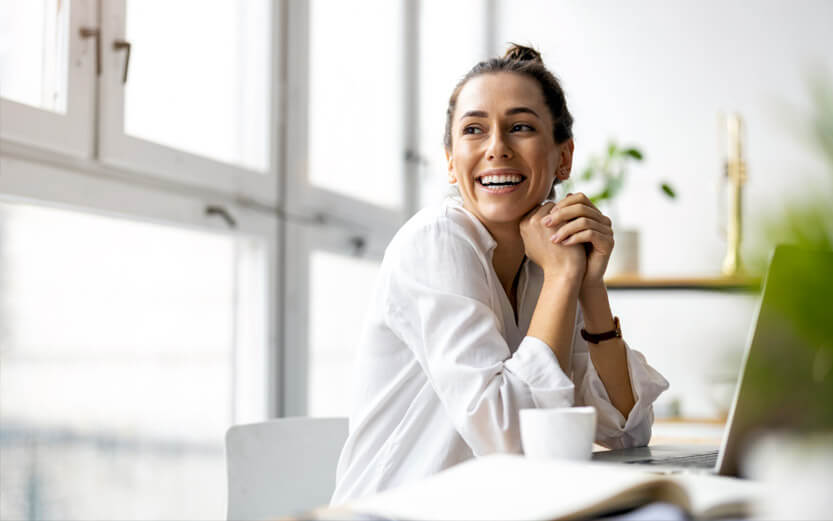 woman with her hair in a bun sitting at a desk smiling