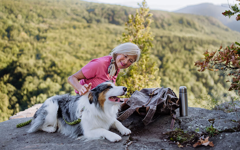 an older woman petting a dog on top of a mountain