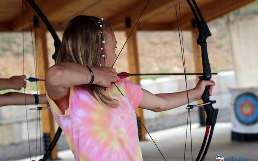 a teen girl wearing a pink tie-dye shirt learning archery