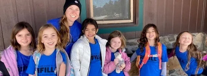 a group of young girls in blue camp t-shirts pose for a photo with their counselor
