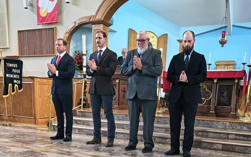 four men standing in front of the church altar with heads lowered in prayer